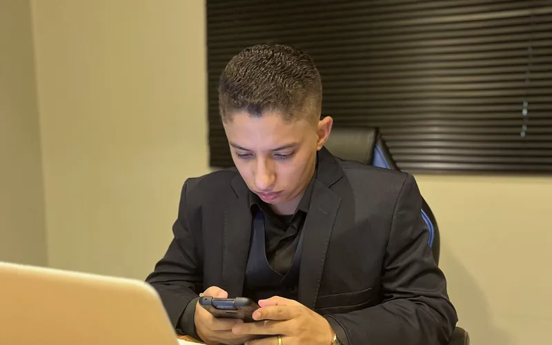 Consultor da EvoluaC respondendo mensagens de clientes no celular, sentado à mesa do escritório