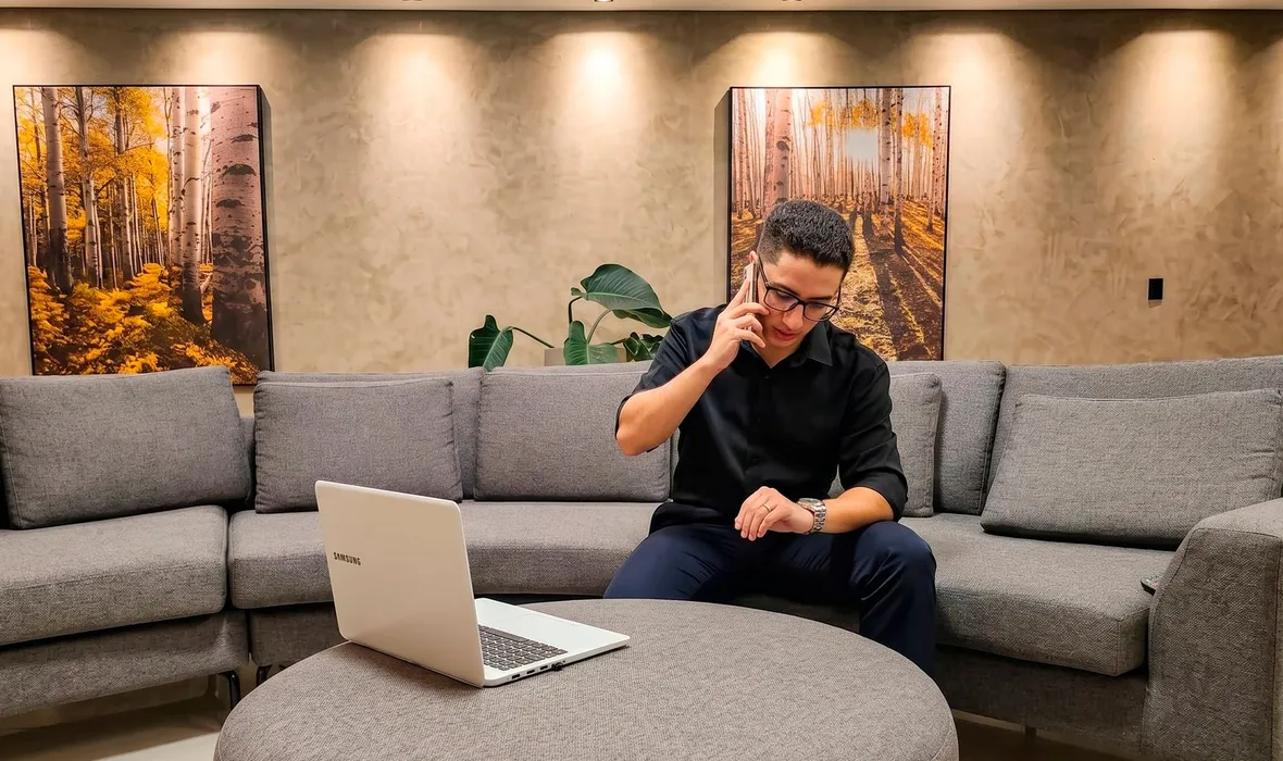 Consultor da EvoluaC falando ao telefone no sofá do escritório, com o notebook na mesa de centro