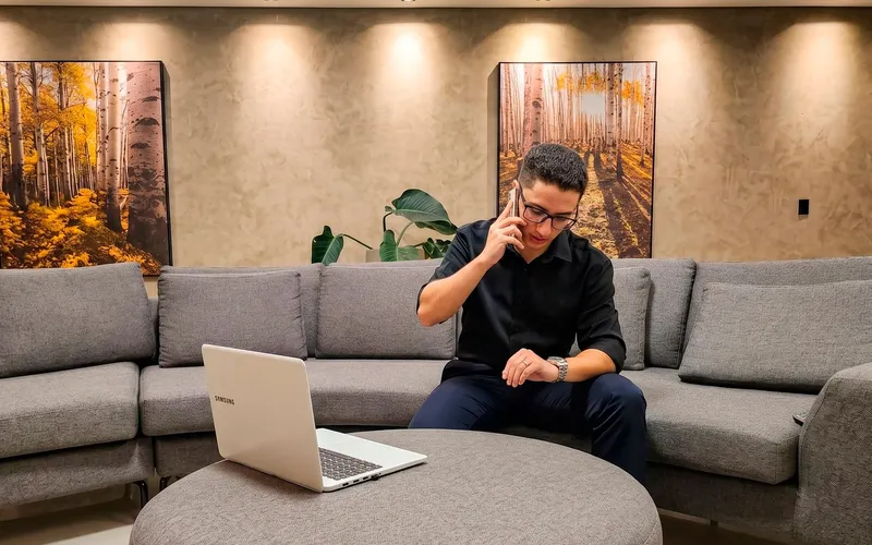 Consultor da EvoluaC falando ao telefone no sofá do escritório, com o notebook na mesa de centro