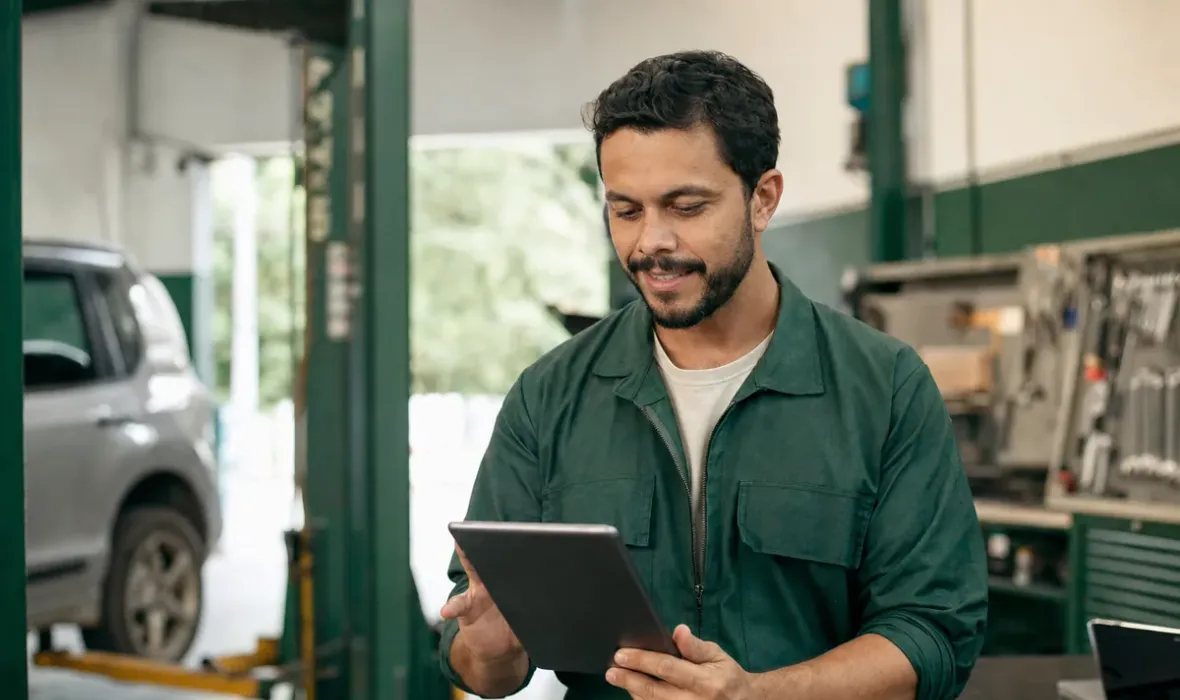 Dono de oficina mecânica conferindo o site da empresa no tablet, com a oficina ao fundo