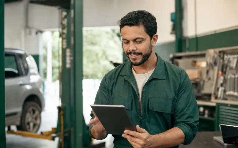 Dono de oficina mecânica conferindo o site da empresa no tablet, com a oficina ao fundo