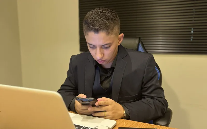 Consultor de marketing respondendo clientes pelo celular, com o notebook aberto
